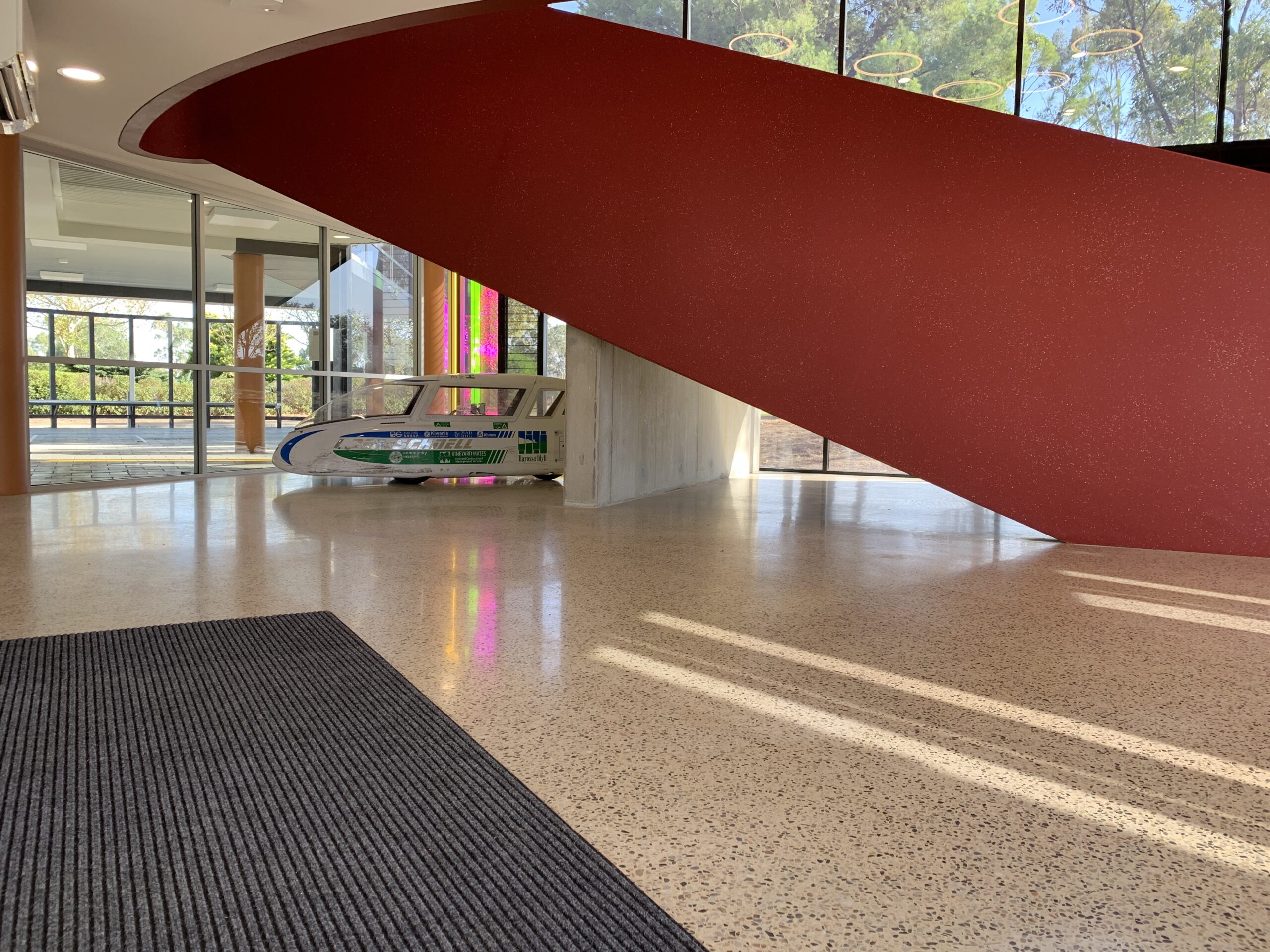Polished concrete floor beneath red curved staircase — Faith Lutheran College foyer