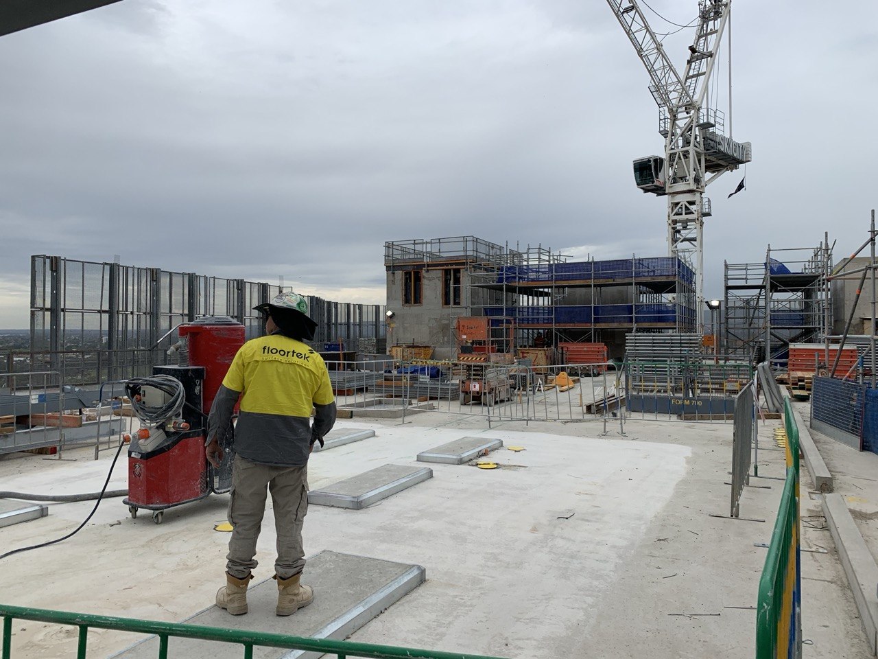 Floortek crew on SkyCity rooftop deck — surface preparation with tower crane in background